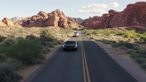 Black-Ferrari-and-white-Rolls-Royce-driving-down-an-open-road-in-the-Valley-of-Fire,-Nevada