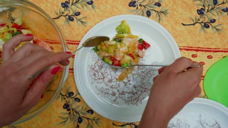 Woman-hands-put-the-salad-on-a-white-plate-in-garden-rural-table-setup,-close-up