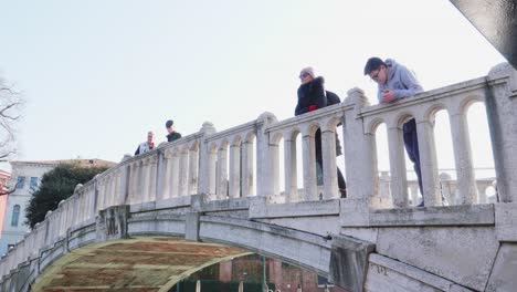 Turistas-Disfrutando-De-La-Vista-Desde-El-Puente-Ponte-Papadopoli,-Sobre-El-Canal-Rio-Novo,-Venecia,-Italia