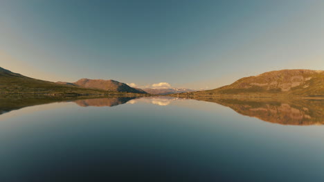 Magnífica-Cordillera-Perfectamente-Reflejada-En-El-Agua-Tranquila-Del-Lago-En-Noruega-Bajo-El-Cielo-Azul-Claro---Amplia-Toma-De-Drones