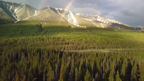 Atemberaubender-Yukon-Flug-Durch-Double-Rainbow-Arc-Und-Malerische-Bergkette-Mit-Grüner,-üppiger-Vegetation-Und-Waldbäumen-Darunter-An-Bewölkten-Tagen,-Kanada,-Seitliche-Luftaufnahmen-über-Dem-Kopf