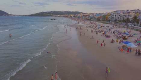 Luftaufnahme-Eines-Dolly-Outs,-Der-Nach-Sonnenuntergang-In-Brasilien-über-Touristen-Am-Strand-Von-Bombas-Fliegt