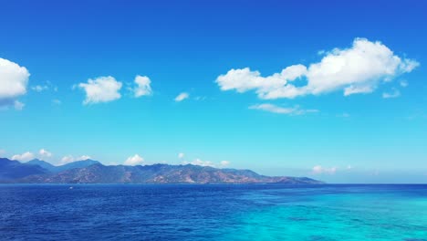 Blue-azure-sea-with-volcanic-high-mountains-horizon-under-bright-sky-with-overhanging-white-clouds-in-Indonesia