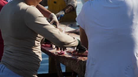 Establishing-shot,-fisherman-and-women-gutting-fish-on-the-table-in-San-Juanico,-Baja-California-Sur,-Mexico,-on-a-sunny-day