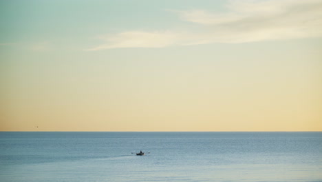 Person-rowing-boat-in-tranquil-calm-sea-waters-at-sunset,-calming-background