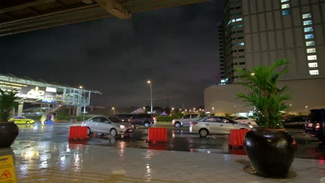 Outdoor-evening-scene-showing-vehicular-traffic-in-a-drizzle-around-a-commercial-district-within-Quezon-City-in-Metro-Manila,-Philippines