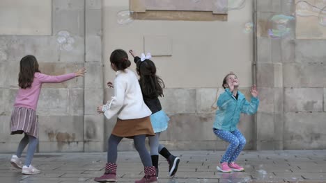 Happy-group-of-girls-having-fun,-enjoying-bursting-soap-bubbles-on-urban-city-street-scene