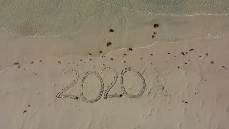 Aerial-camera-descending-on-Twenty-Twenty-inscribed-in-the-sand-on-a-beach