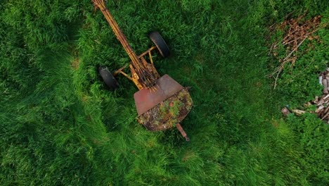 Rising-overhead-shot,-old-excavator-and-junk-in-overgrown-green-field