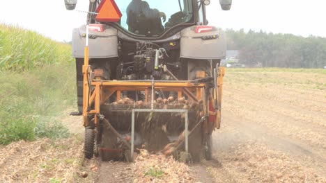 Nahaufnahme-Einer-Maschine-Hinter-Einem-Traktor,-Die-Zwiebeln-Erntet,-Von-Hinten-Gesehen,-Die-Die-Ernte-Vom-Erntebereiten-Boden-Trennt