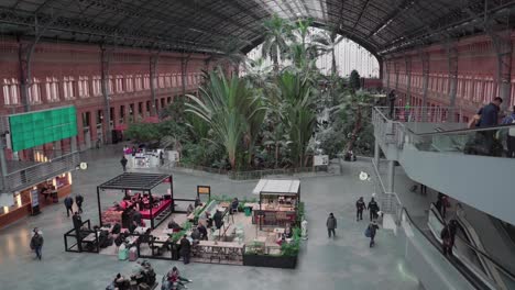 Vista-Panorámica-En-El-Vestíbulo-De-La-Estación-De-Tren-De-Atocha-En-Madrid,-España-Con-Viajeros-Caminando-Y-Montando-En-Travellator---ángulo-Alto,-Tiro-Panorámico