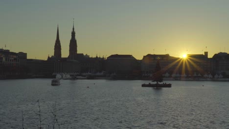 Blick-Auf-Den-Sonnenuntergang-über-Hamburg,-Deutschland,-über-Die-Binnenalster-Mit-Einem-Ausflugsboot,-Das-Im-Dezember-2019-An-Einem-Schwimmenden-Weihnachtsbaum-Vorbeifährt