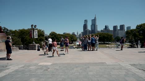 Gruppe-Von-Menschen,-Die-Fotos-An-Den-Felsigen-Stufen-In-Pennsylvania-Machen-–-Washington-Monument-Fountain-Und-Die-Skyline-Von-Philadelphia-Im-Hintergrund-–-Zeitraffer,-Totalaufnahme