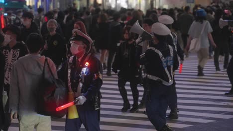 Eine-Gruppe-Maskierter-Polizisten-Hält-Ein-Megafon-In-Der-Hand-Und-Führt-Einen-Schlagstock,-Der-Die-Menge-Am-Shibuya-Kreuz-In-Der-Halloween-Nacht-2020-Kontrolliert---Zeitlupe