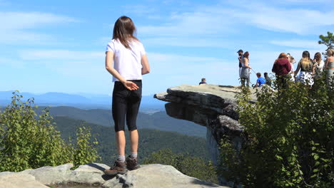 A-girl-looks-at-people-standing-on-McAfee-Knob-taking-photos,-she-stands-up-and-sits-back-down