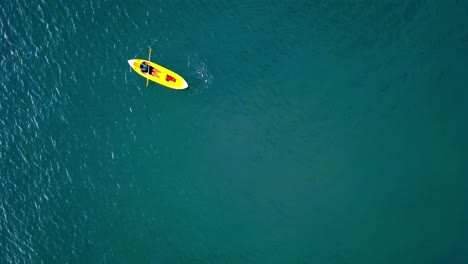 Aerial-top-down-shot-of-an-unrecognizable-man-rowing-on-a-kayak-on-turquoise-color-water