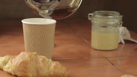 Pouring-fresh-coffee-into-cup-with-croissant-pastry-medium-shot