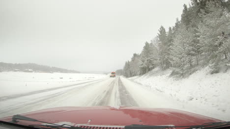 A-snow-plough-clears-a-snowy-winter-road-in-Sweden,-wide-dashboard-cam-shot