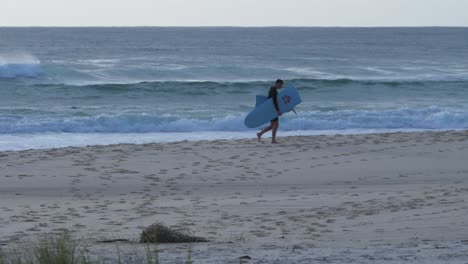 Männlicher-Surfer-Verlässt-Den-Strand-Mit-Kaputtem-Surfbrett-–-Palmenstrand-Mit-Meereswellen-–-New-South-Wales,-Australien