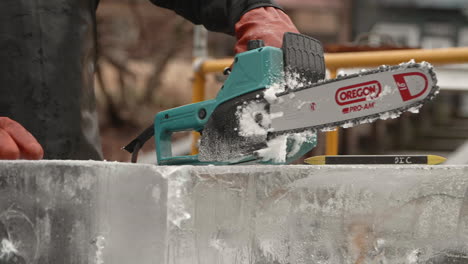 Ice-sculptor-resting-chainsaw-on-ice-block-with-falling-snow,-Slow-Motion