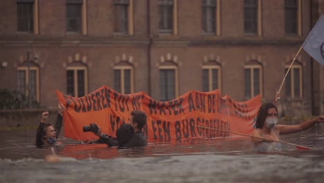 Activistas-Con-Pancartas-En-El-Agua-Para-Llamar-La-Atención-Sobre-El-Cambio-Climático-Y-El-Aumento-Del-Nivel-Del-Mar-Durante-La-Protesta-De-La-Rebelión-De-Extinción-Frente-Al-Parlamento-De-La-Haya,-Países-Bajos---Hofvijver,-Slowmo