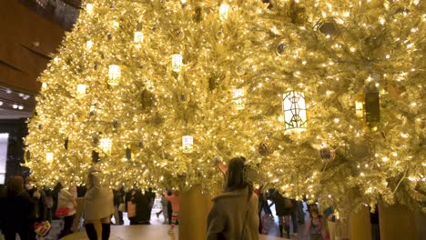 Una-Mujer-Celebra-Las-Vacaciones-De-Navidad-Mientras-Posa-Frente-A-Un-árbol-De-Navidad-Dorado-En-Un-Centro-Comercial-En-Hong-Kong