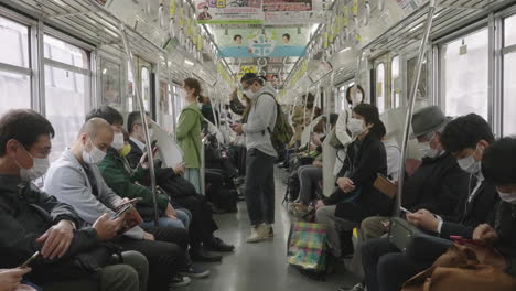Viajeros-Japoneses-Con-Máscaras-Dentro-De-Un-Tren-En-Movimiento-En-Tokio,-Japón---Nuevo-Protocolo-De-Salud-Normal---Toma-Estática,-Cámara-Lenta