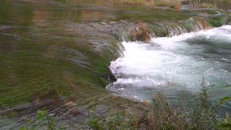 Close-up-of-a-strong-current-of-water-flowing-from-one-pond-down-to-another-submerging-the-grass-nearby-at-¼-speed