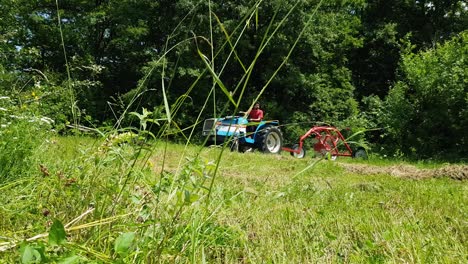 Agricultor-Conduciendo-Tractor-Con-Henificador-Adjunto-En-Las-Tierras-De-Cultivo-En-Omurtag,-Bulgaria---Disparo-De-Bajo-Nivel