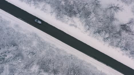 A-car-ist-driving-through-a-winter-landscape,-top-shot-with-a-straight-diagonal-leading-road,-made-by-a-drone-at-4k