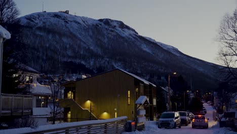 Cars-driving-on-snowy-road-through-housing-area-in-Tromso-District-during-blue-hour