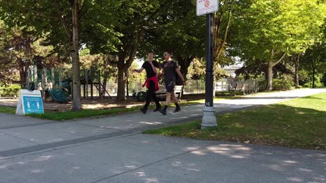 law-breaking-young-adult-males-unmasked-walk-in-close-range-of-each-other-ignoring-the-restrictions-of-COVID-19-during-lockdown-pandemic-at-city-park-with-vintage-light-posts-benches-empty-playground