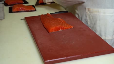 White-coated-fish-industry-worker-cutting-and-packing-smoked-salmon-fillets---static-slow-motion