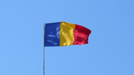 Bandera-Tricolor-Rumana-Ondeando-En-El-Viento,-Fondo-De-Cielo-Azul