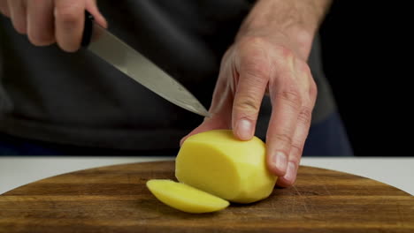 Chef-cutting-and-slicing-peeled-potato-on-chopping-board,-closeup