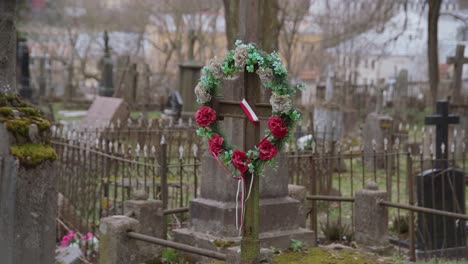 Old-Rusty-Metal-Cross-with-Artificial-Flower-Wreath-and-Ribbon-Polish-Flag-in-Old-Graveyard