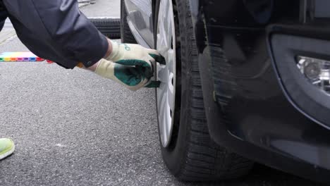 Working-man-removes-hubcaps-on-a-black-car,-closeup