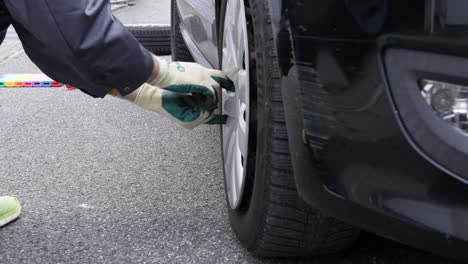 Hombre-De-Trabajo-Quita-Tapacubos-En-Un-Coche-Negro,-Primer-Plano