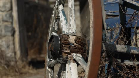 Gorgeous-closeup-of-a-patinaed-old-wagon-wheel-and-frame-outside-with-a-old-stone-farm-building-in-the-background-in-Gatineau,-Quebec