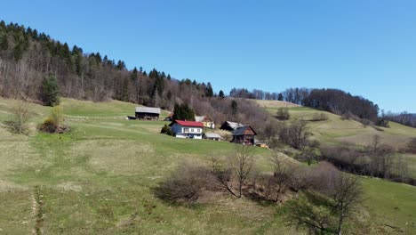 Aerial-approaching-rustic-houses-on-hill-against-blue-sky-on-a-sunny-day,-Lasko,-Slovenia