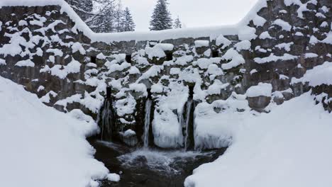 Concrete-wall-or-dam-with-three-spillway-pipes-at-bottom-covered-in-snow