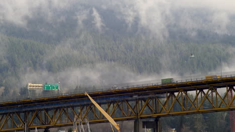Motion-Timelapse-Of-Vehicles-And-Clouds-By-The-Ironworkers-Memorial-Bridge-In-Vancouver,-BC,-Canada-With-Lush-Forest-Mountain-In-Background