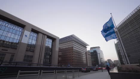 Banderas-De-La-Ue-Ondeando-Frente-A-La-Comisión-Europea-Mientras-Un-Peatón-Solitario-Pasa,-Bruselas