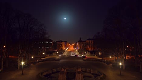 Timelapse-of-Munich-at-night,-view-from-the-Friedensengel-Europaplatz-at-driving-cars,-stopping-at-red-traffic-lights,-accelerating---stop-and-go-under-the-full-moon