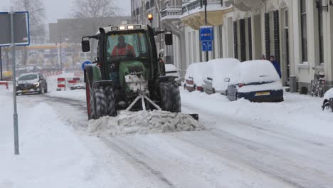 Large-green-tractor-with-a-shovel-in-front-clearing-the-road-of-excess-snow-from-a-heavy-snowstorm-in-The-Netherlands