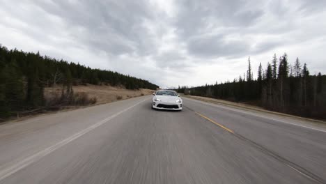 Sporty-White-Car-Chasing-Low-Flying-Drone-On-Highway