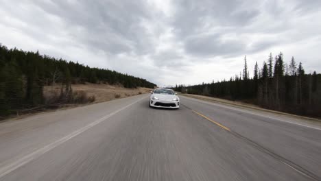 Coche-Blanco-Deportivo-Persiguiendo-Drones-De-Bajo-Vuelo-En-La-Carretera