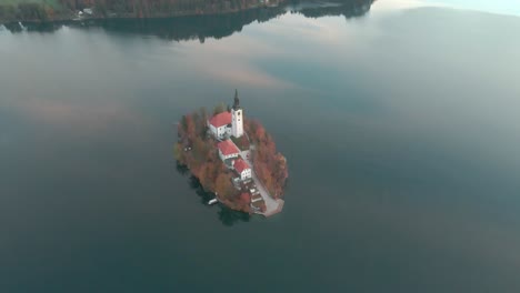 Insel-Bleder-See-In-Slowenien,-Wobei-Die-Drohne-Frühmorgens-Auf-Die-Insel-Zufliegt-Und-Die-Kamera-Auf-Die-Insel-Selbst-Herunterrollt