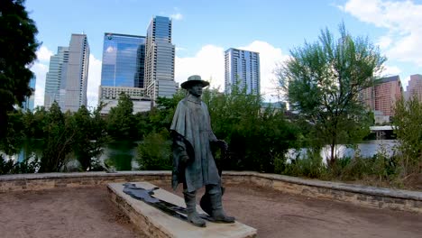 Ein-Sanfter,-Stetiger-Clip-Der-Stevie-Ray-Vaughan-Statue-Am-Ufer-Des-Lady-Bird-Lake-Mit-Der-Skyline-Von-Austin-Im-Hintergrund