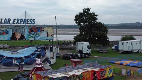 Empty-overcast-British-amusement-park-aerial-view-deserted-funfair-rides-slow-right-pull-back-rising